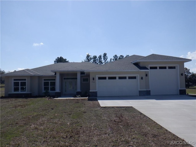 prairie-style home featuring a front lawn, a garage, driveway, and stucco siding