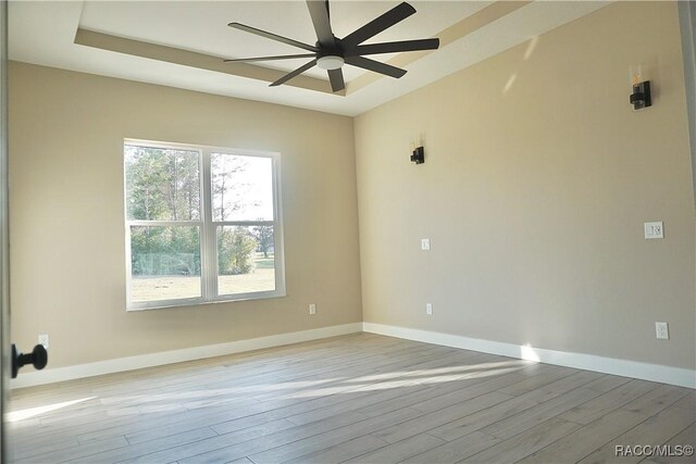 empty room with a tray ceiling, baseboards, wood finished floors, and a ceiling fan