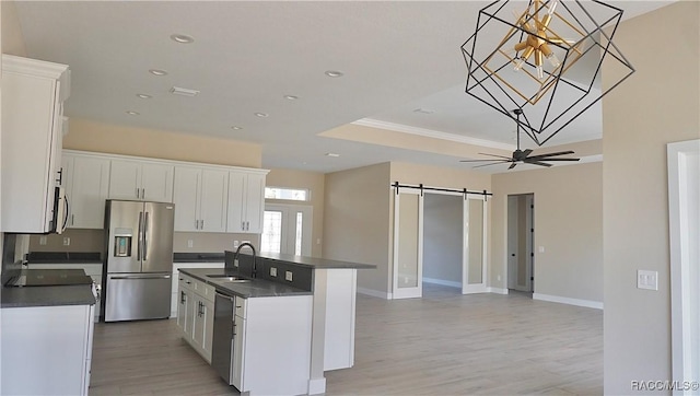 kitchen with dark countertops, a sink, ceiling fan, stainless steel appliances, and a barn door