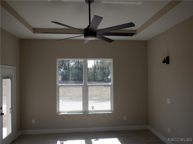 empty room with a ceiling fan, a raised ceiling, wood finished floors, and baseboards