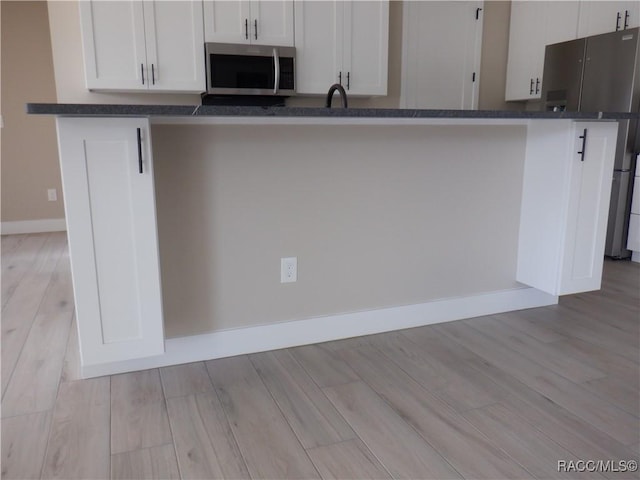 kitchen with appliances with stainless steel finishes, white cabinetry, light wood-type flooring, and baseboards