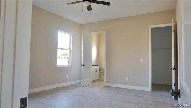 unfurnished bedroom with light wood-type flooring, ensuite bathroom, a closet, baseboards, and a spacious closet