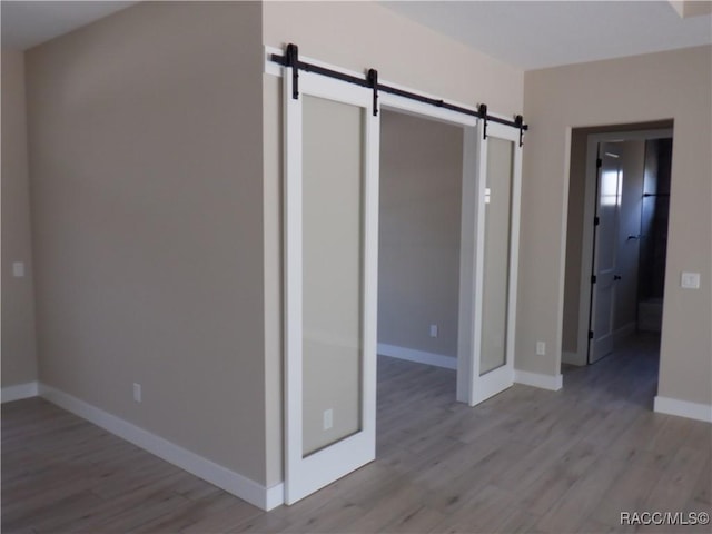 unfurnished bedroom featuring baseboards, a barn door, and wood finished floors