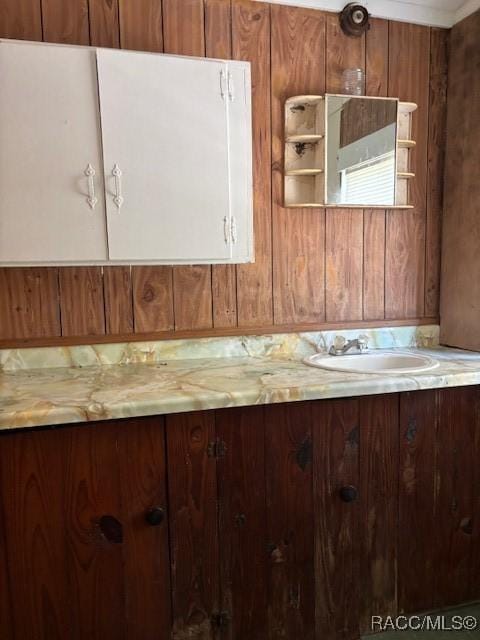 kitchen featuring brown cabinetry, a sink, wood walls, and open shelves