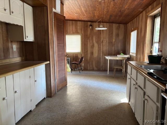 kitchen with wooden ceiling, wooden walls, a sink, white cabinets, and hanging light fixtures