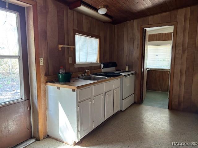 kitchen featuring white gas stove, white cabinets, wood walls, a sink, and wooden ceiling