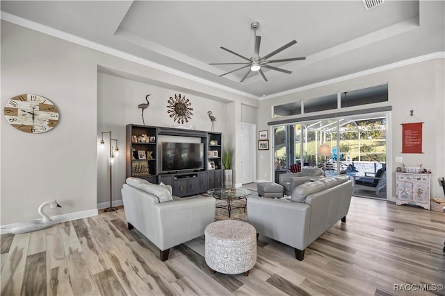 living room featuring ceiling fan, a raised ceiling, wood-type flooring, and crown molding