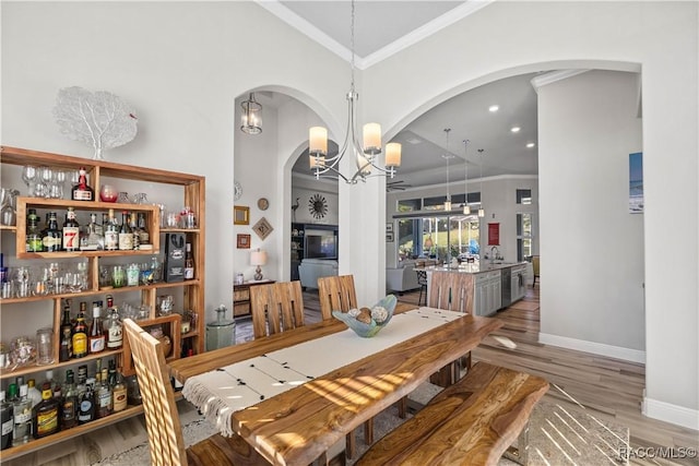 dining space with wood-type flooring, bar, ornamental molding, and a notable chandelier