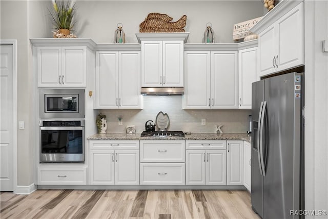 kitchen with white cabinets, stainless steel appliances, light stone counters, and light hardwood / wood-style floors