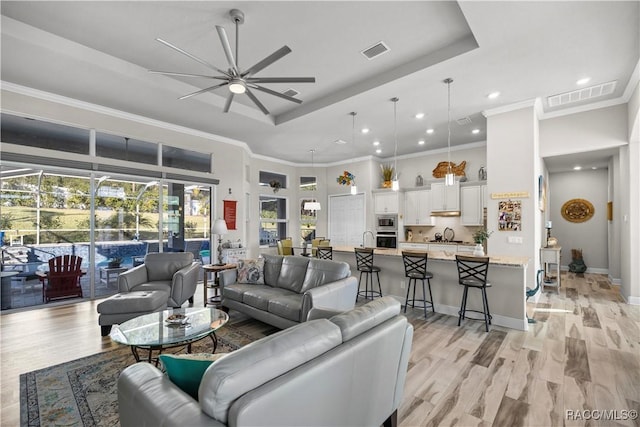 living room with ceiling fan, light hardwood / wood-style floors, crown molding, and a tray ceiling