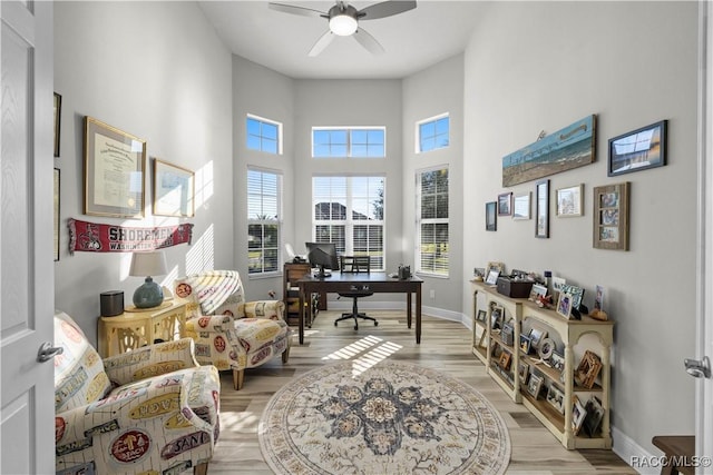 home office with a towering ceiling, light hardwood / wood-style flooring, and ceiling fan