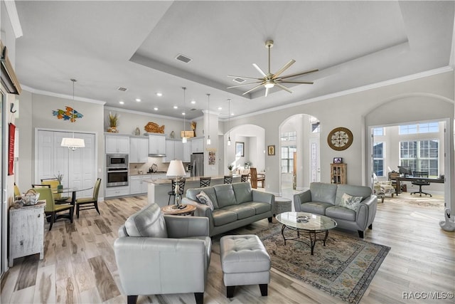 living room featuring a tray ceiling, ornamental molding, and light wood-type flooring