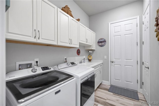 clothes washing area featuring washer and clothes dryer, cabinets, light wood-type flooring, and sink