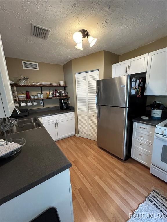 18 56th St, Yankeetown, FL 34498 - kitchen featuring freestanding refrigerator, light wood-style floors, white cabinetry, dark countertops, and a textured ceiling