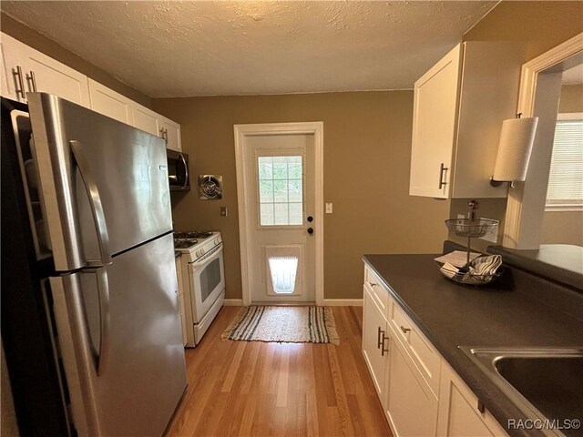 18 56th St, Yankeetown, FL 34498 - kitchen featuring stainless steel appliances, light wood-style flooring, white cabinetry, dark countertops, and a textured ceiling