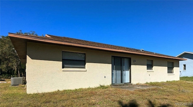 back of house featuring stucco siding, central AC, and a yard