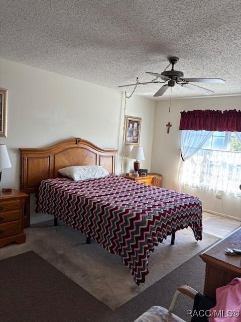 carpeted bedroom with ceiling fan and a textured ceiling