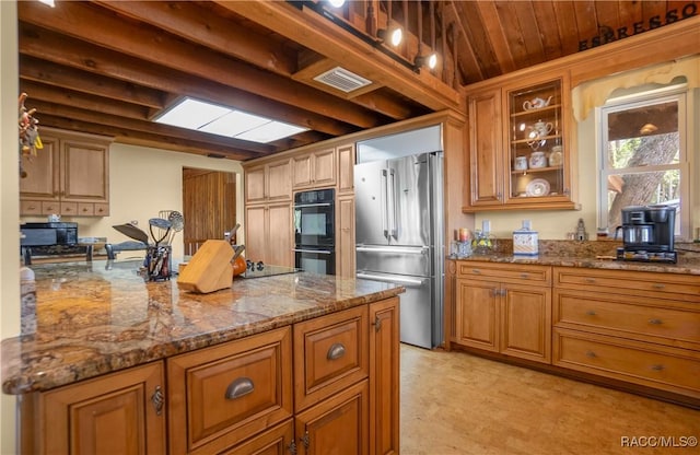 kitchen featuring stone countertops, visible vents, black appliances, brown cabinetry, and glass insert cabinets