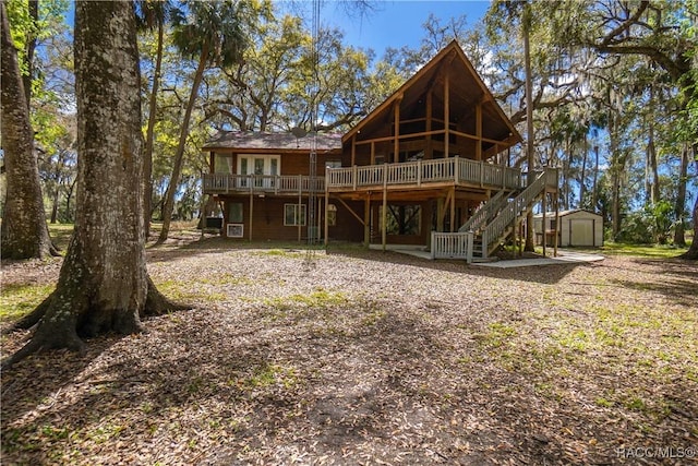 back of property with stairway, a wooden deck, a storage unit, and an outdoor structure