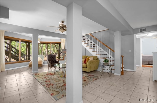 living area featuring light tile patterned floors, visible vents, baseboards, ceiling fan, and stairway