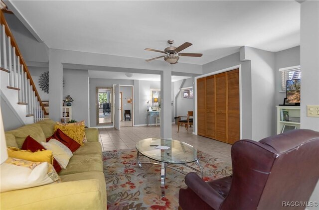 living area with stairs, a ceiling fan, and tile patterned floors