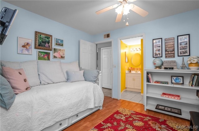 bedroom featuring ensuite bath, wood finished floors, visible vents, and a ceiling fan