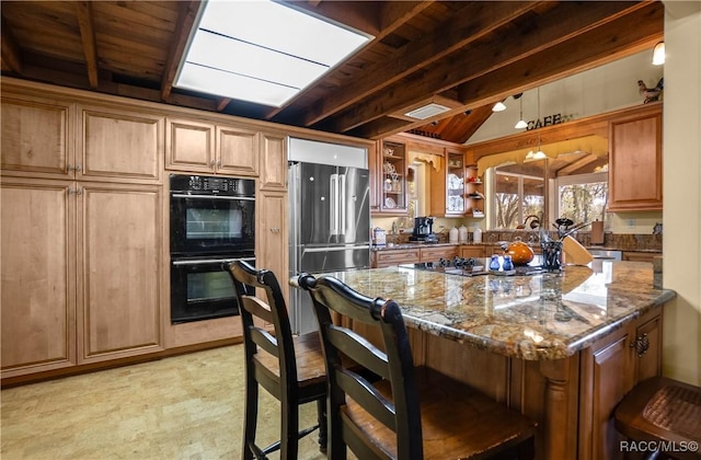 kitchen featuring freestanding refrigerator, dobule oven black, a kitchen breakfast bar, and dark stone countertops