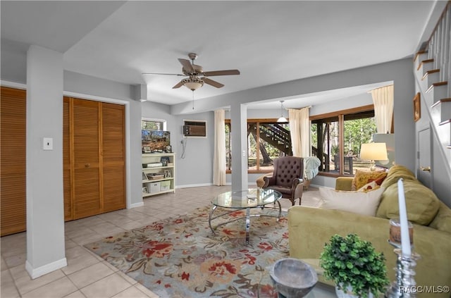 tiled living room with an AC wall unit, a ceiling fan, and baseboards