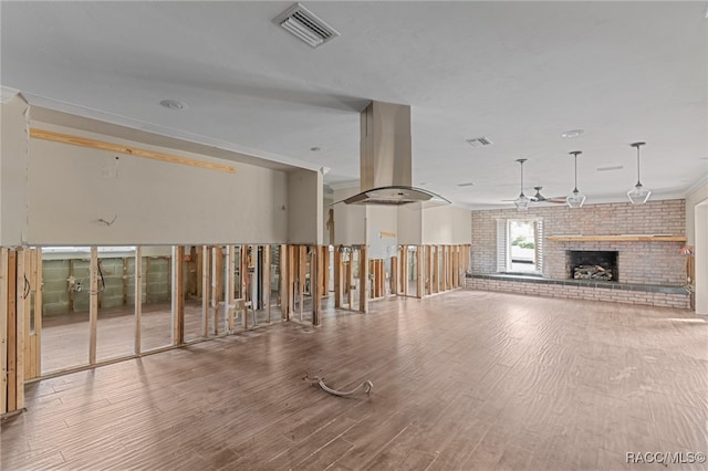 unfurnished living room featuring hardwood / wood-style floors, ceiling fan, a fireplace, and brick wall