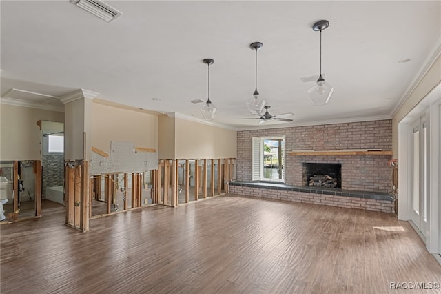 unfurnished living room with hardwood / wood-style floors, crown molding, a brick fireplace, ceiling fan, and brick wall