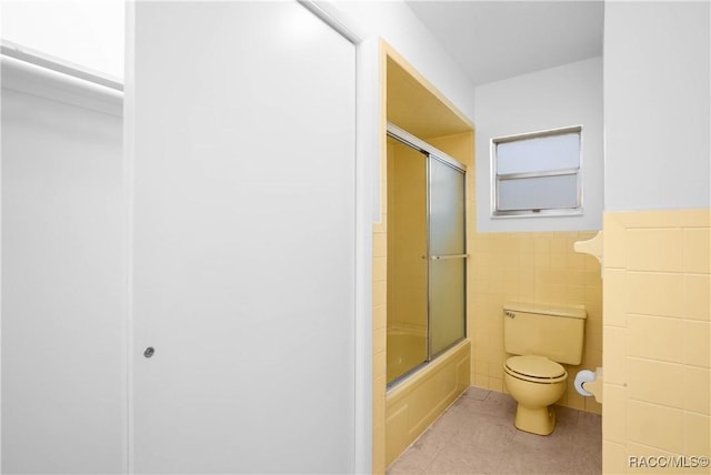 bathroom featuring tile walls, shower / bath combination with glass door, and toilet