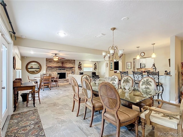 dining space featuring a textured ceiling, ceiling fan with notable chandelier, and a brick fireplace