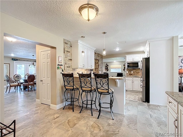 kitchen featuring a breakfast bar area, kitchen peninsula, tasteful backsplash, and white cabinets