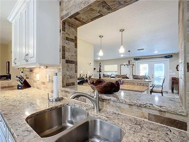 kitchen with light stone countertops, sink, tasteful backsplash, decorative light fixtures, and white cabinets