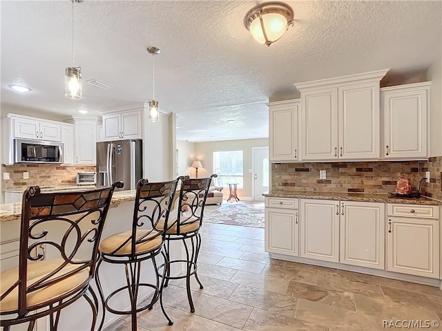 kitchen with pendant lighting, backsplash, stainless steel appliances, and light stone counters