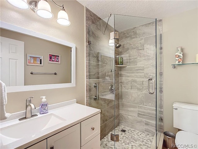 bathroom featuring toilet, vanity, a textured ceiling, and walk in shower