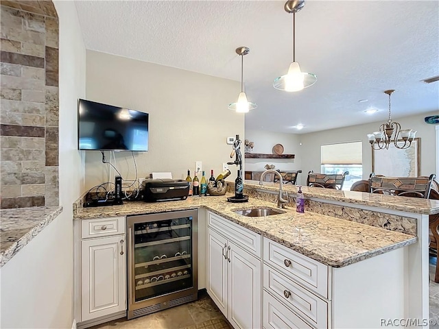 kitchen featuring wine cooler, light stone countertops, sink, and pendant lighting