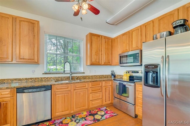 kitchen with sink, ceiling fan, light stone countertops, light hardwood / wood-style floors, and stainless steel appliances