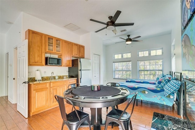 kitchen with light stone counters, ceiling fan, sink, white refrigerator, and light hardwood / wood-style floors