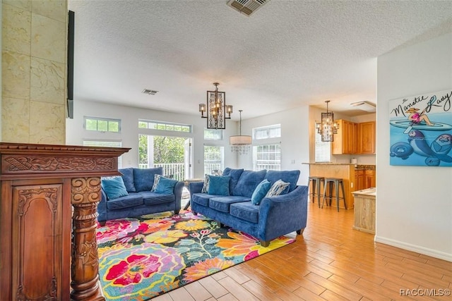 living room featuring light hardwood / wood-style flooring, a textured ceiling, and a notable chandelier