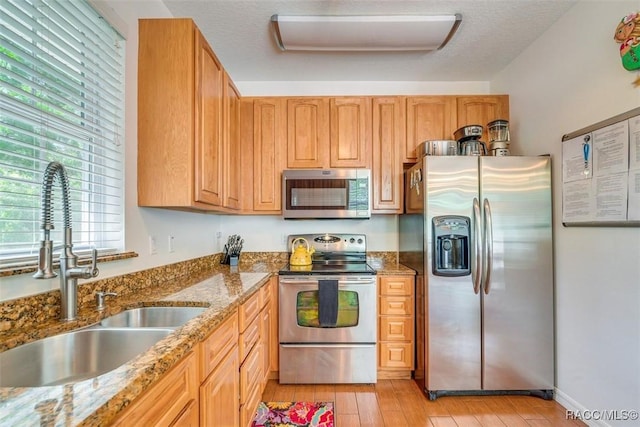 kitchen featuring sink, light stone countertops, a textured ceiling, appliances with stainless steel finishes, and light hardwood / wood-style floors