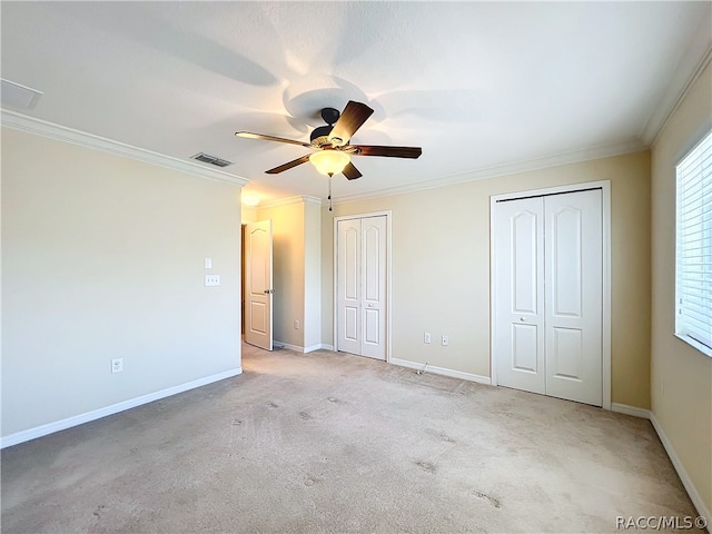 unfurnished bedroom featuring multiple closets, ceiling fan, crown molding, and light colored carpet