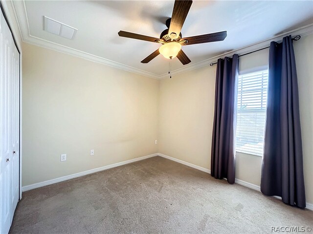 carpeted spare room featuring ceiling fan and crown molding