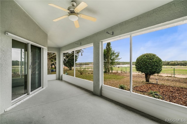 unfurnished sunroom with lofted ceiling, a rural view, and a ceiling fan