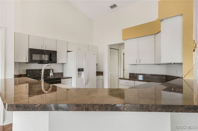 kitchen featuring visible vents, a high ceiling, dark stone counters, a peninsula, and black appliances