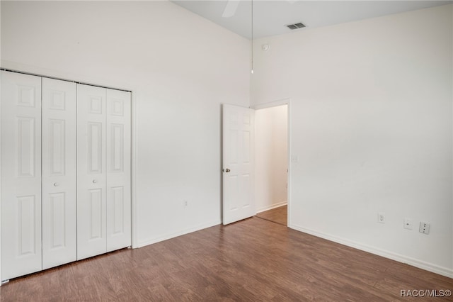 unfurnished bedroom with baseboards, visible vents, a towering ceiling, wood finished floors, and a closet