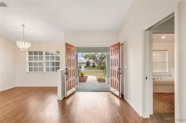 foyer entrance with visible vents, a notable chandelier, baseboards, and wood finished floors