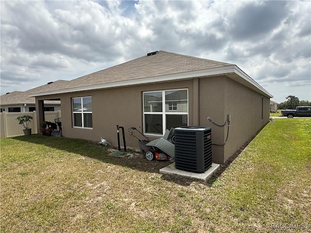 rear view of property with central AC, fence, a yard, stucco siding, and roof with shingles