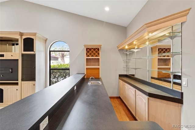 bar with light brown cabinets, lofted ceiling, sink, and light hardwood / wood-style flooring