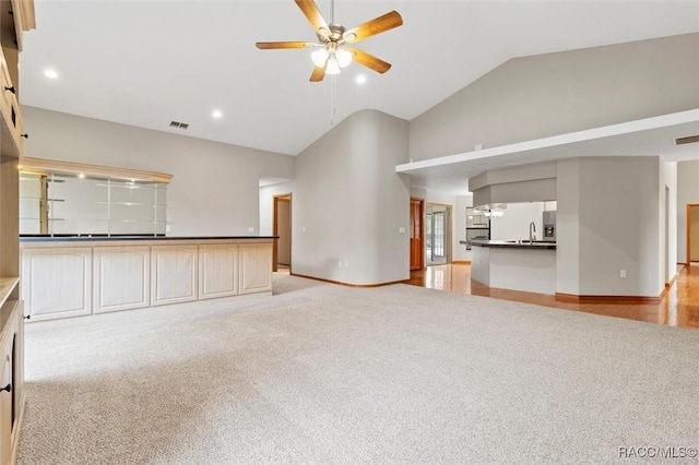 unfurnished living room with light carpet, ceiling fan, and high vaulted ceiling